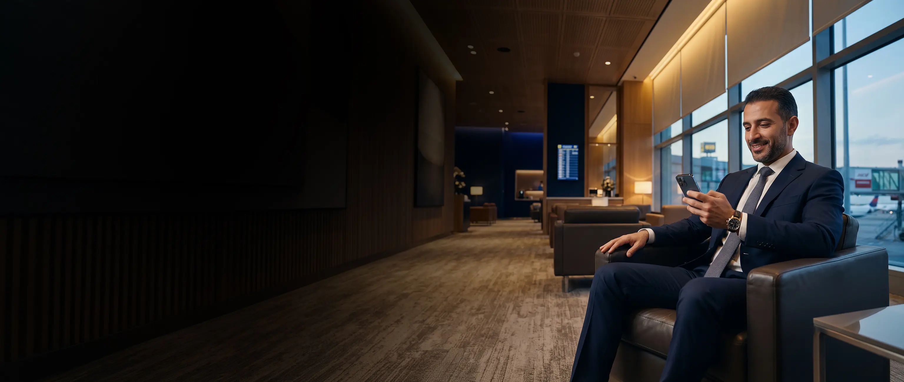 A smiling professional managing his National Bonds Prestige Silver account on a smartphone while relaxing in an exclusive airport lounge.